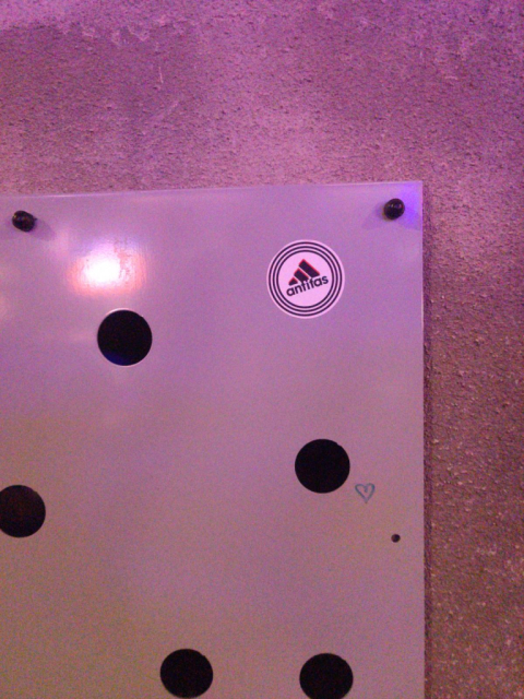 Photo of a metal plate with holes in it, attached to a house wall.<br>There is an antifa sticker stuck to it, shaped like the logo of a well known sports brand.